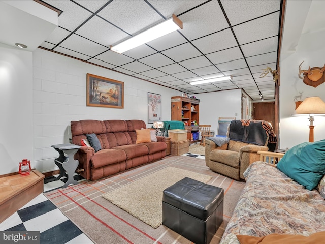 living room featuring a drop ceiling and concrete block wall