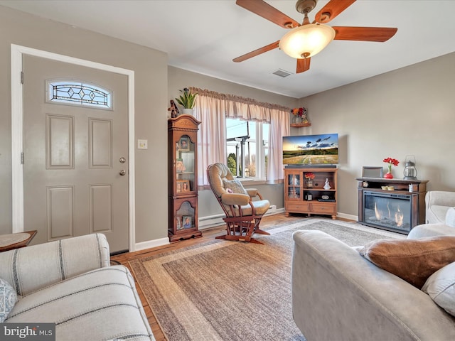 living room featuring visible vents, a glass covered fireplace, light wood-style floors, a baseboard radiator, and baseboards