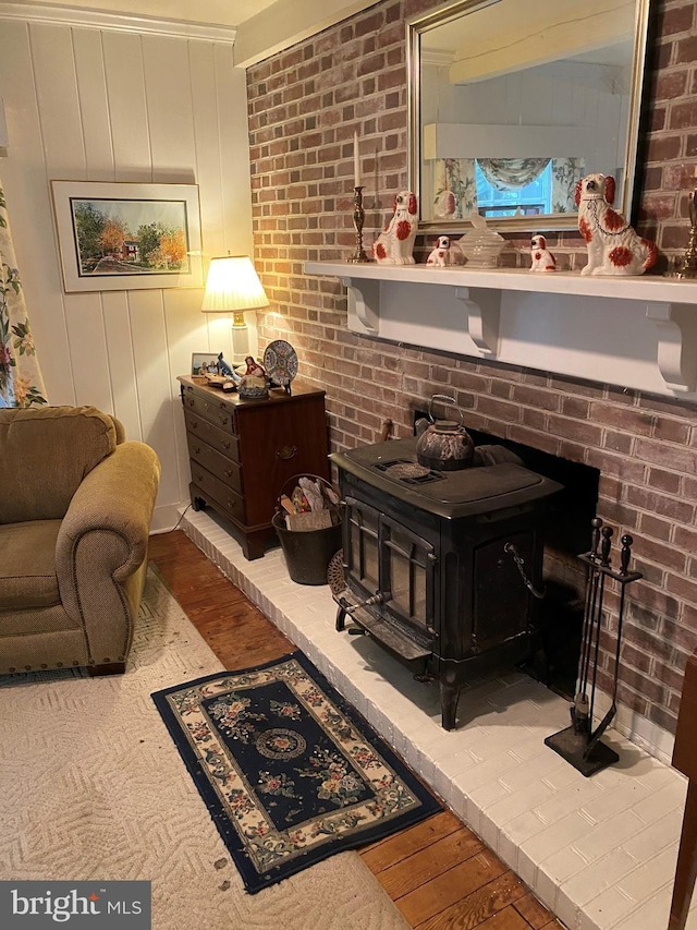 living area featuring a wood stove, wood finished floors, and brick wall