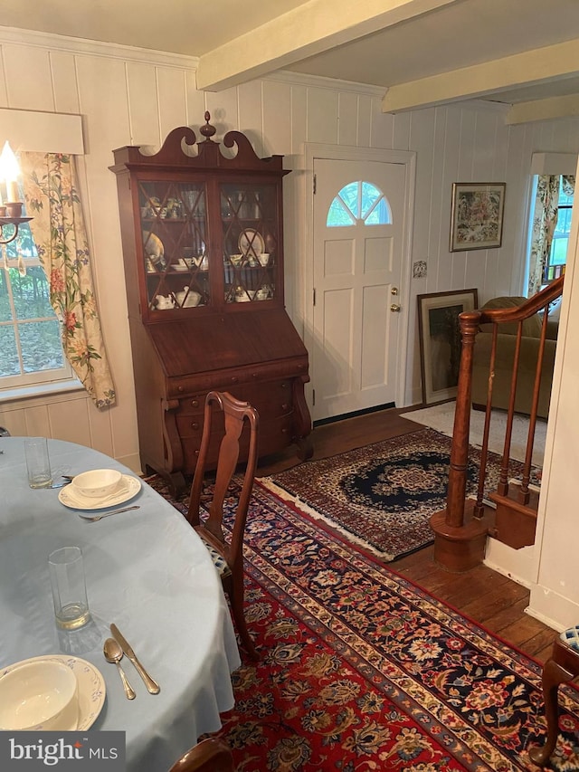 dining area featuring beam ceiling, a healthy amount of sunlight, stairs, and wood finished floors