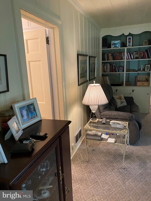 sitting room featuring visible vents, built in shelves, carpet flooring, and crown molding