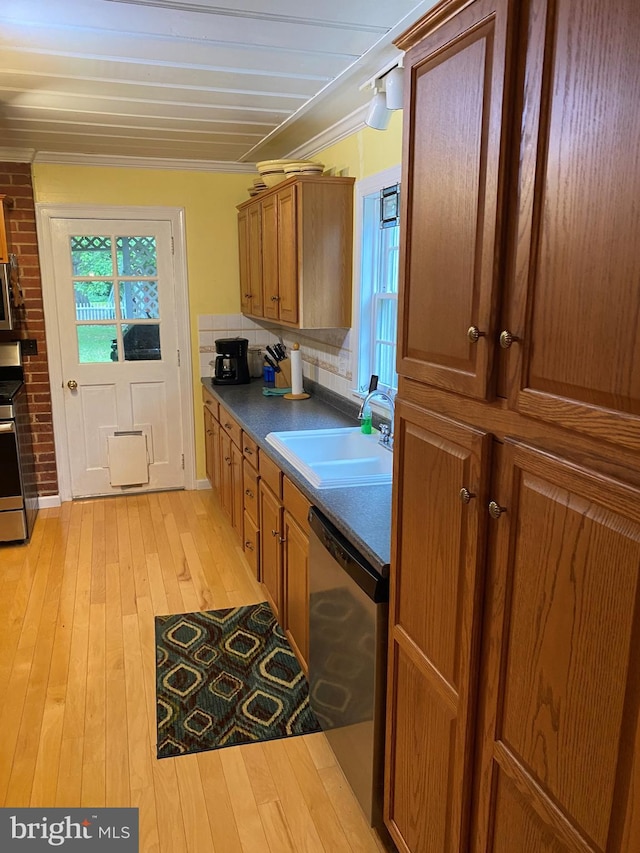 kitchen with brown cabinetry, light wood finished floors, a sink, appliances with stainless steel finishes, and crown molding