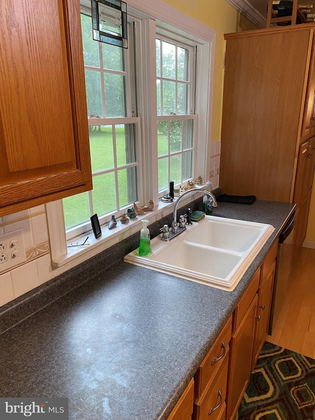 kitchen with a sink, stainless steel dishwasher, dark countertops, and brown cabinetry