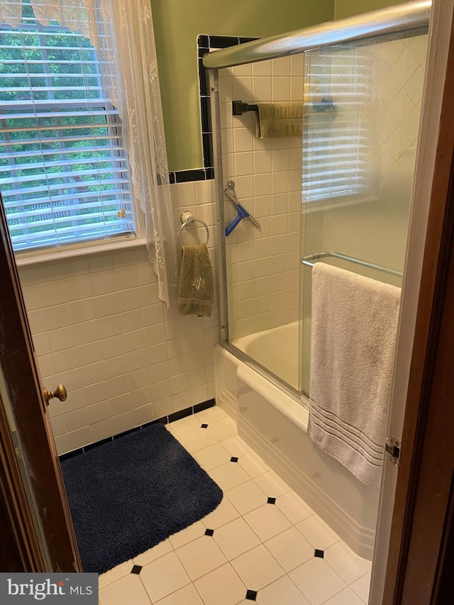 bathroom featuring tile patterned floors, tile walls, and combined bath / shower with glass door