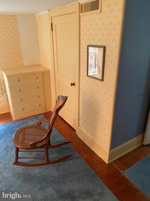 living area with wallpapered walls, dark wood-type flooring, baseboards, and visible vents