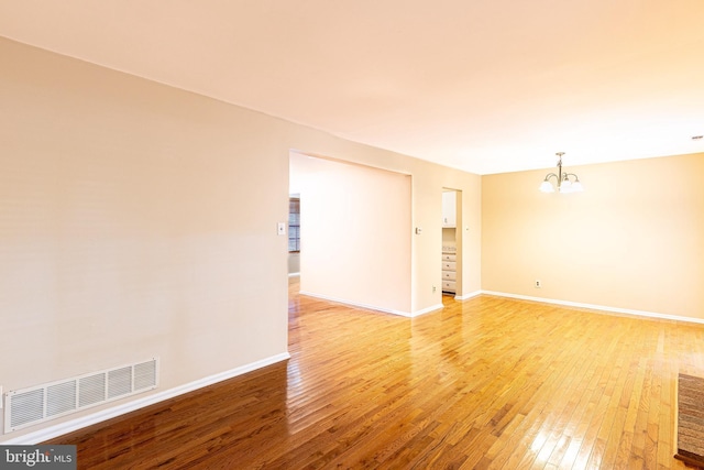 spare room with an inviting chandelier, light wood-style flooring, baseboards, and visible vents