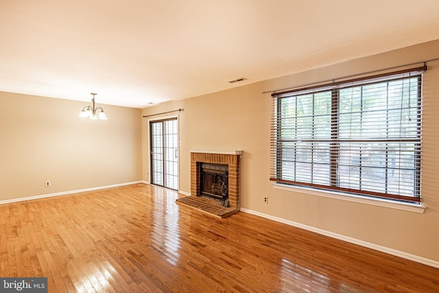 unfurnished living room with visible vents, a notable chandelier, hardwood / wood-style floors, a fireplace, and baseboards