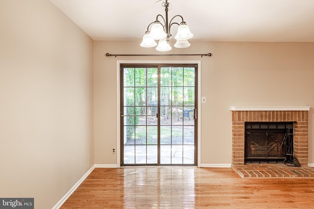 unfurnished living room with a chandelier, baseboards, a brick fireplace, and wood finished floors