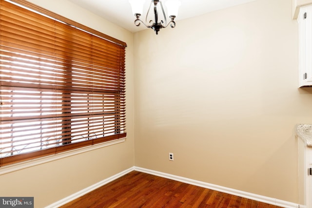 unfurnished room featuring baseboards, an inviting chandelier, and dark wood-style flooring