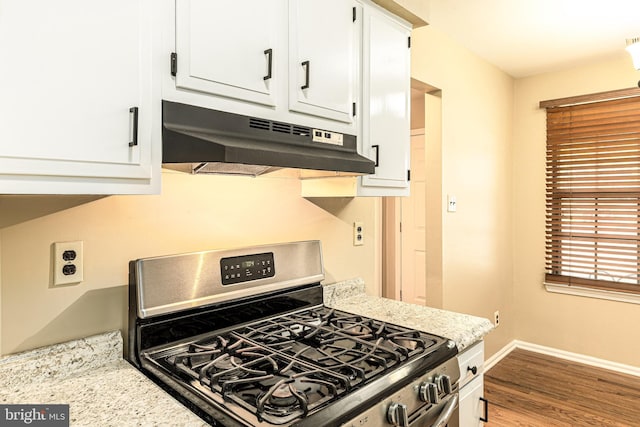 kitchen featuring under cabinet range hood, wood finished floors, gas range, white cabinets, and baseboards