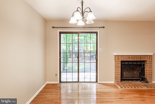 unfurnished living room featuring a fireplace, a notable chandelier, wood finished floors, and baseboards