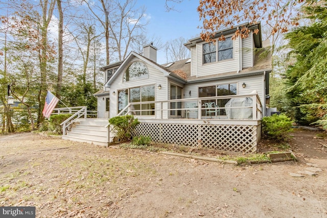 rear view of property featuring a wooden deck, roof with shingles, and a chimney