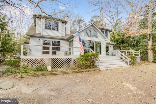 view of front of home with a chimney, a wooden deck, and roof with shingles