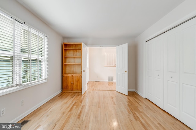 unfurnished bedroom with light wood-type flooring, a closet, baseboards, and visible vents