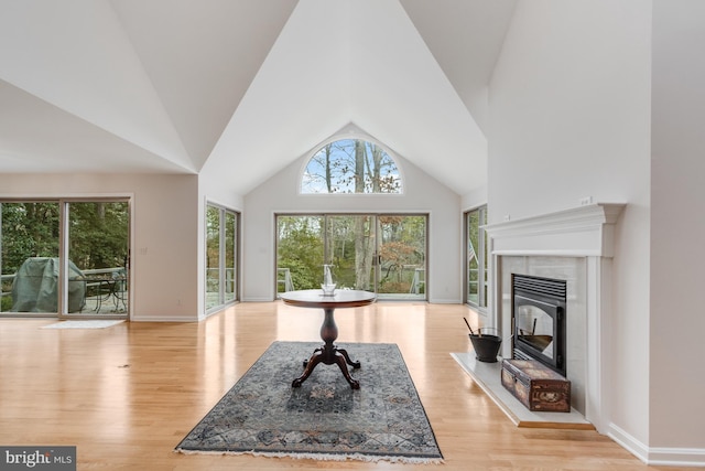 living room with a wealth of natural light, a fireplace, high vaulted ceiling, and wood finished floors