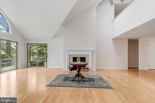 living area featuring a fireplace with flush hearth, high vaulted ceiling, baseboards, and wood finished floors