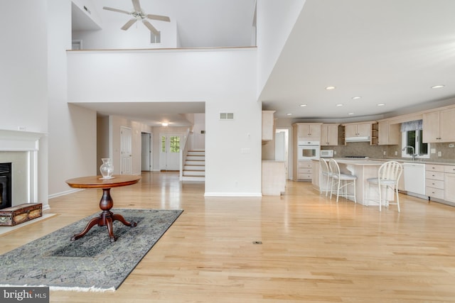 living area with stairway, light wood-style flooring, a healthy amount of sunlight, and ceiling fan