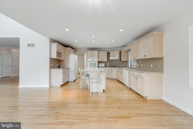 kitchen with visible vents, light countertops, light wood-style flooring, a kitchen breakfast bar, and white appliances