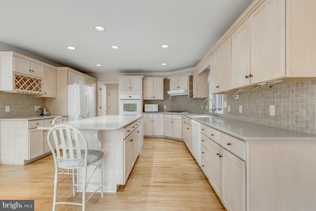 kitchen featuring white appliances, light wood finished floors, a sink, under cabinet range hood, and a center island