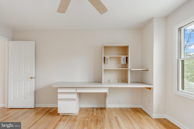 unfurnished office featuring baseboards, a ceiling fan, light wood-style flooring, and built in desk