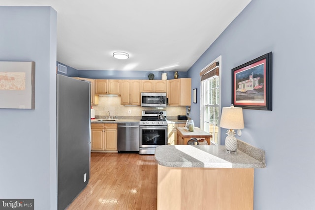 kitchen featuring light wood-style flooring, light brown cabinetry, stainless steel appliances, light countertops, and decorative backsplash