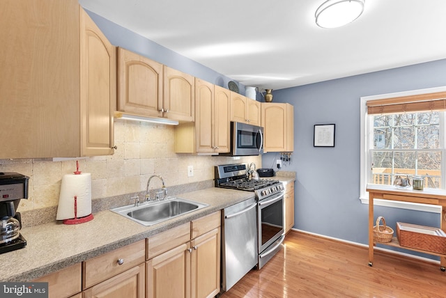 kitchen with light wood finished floors, light brown cabinetry, decorative backsplash, appliances with stainless steel finishes, and a sink