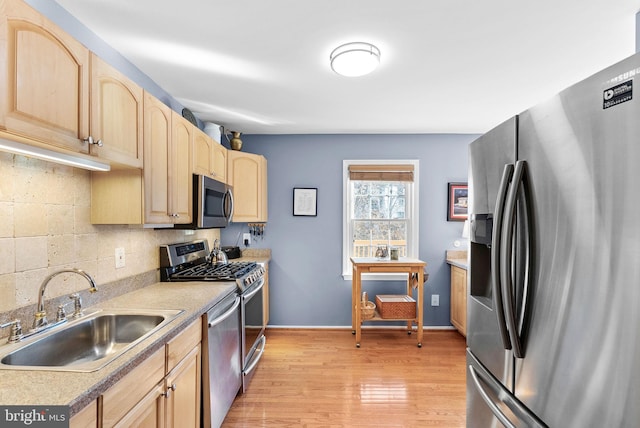 kitchen featuring light brown cabinetry, a sink, backsplash, light wood-style floors, and appliances with stainless steel finishes