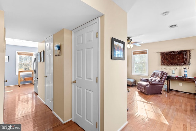 hallway with visible vents, a healthy amount of sunlight, and light wood-style floors