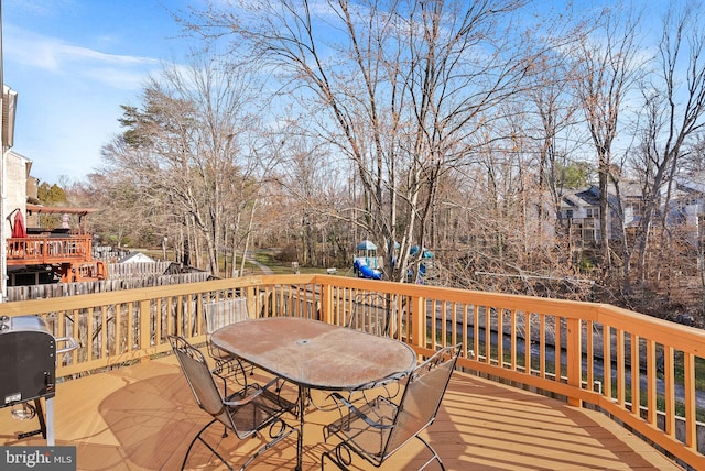 wooden deck with outdoor dining space, a playground, and area for grilling