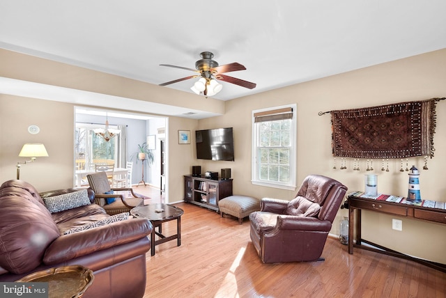 living room featuring ceiling fan with notable chandelier, light wood-style floors, and baseboards