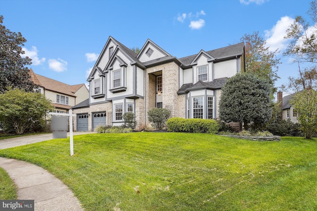 english style home featuring a front lawn, driveway, stone siding, an attached garage, and stucco siding