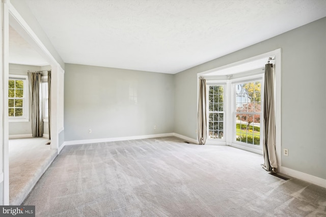carpeted empty room featuring a textured ceiling, a healthy amount of sunlight, and baseboards