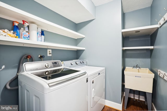 clothes washing area featuring washer and clothes dryer, laundry area, wood finished floors, a sink, and baseboards