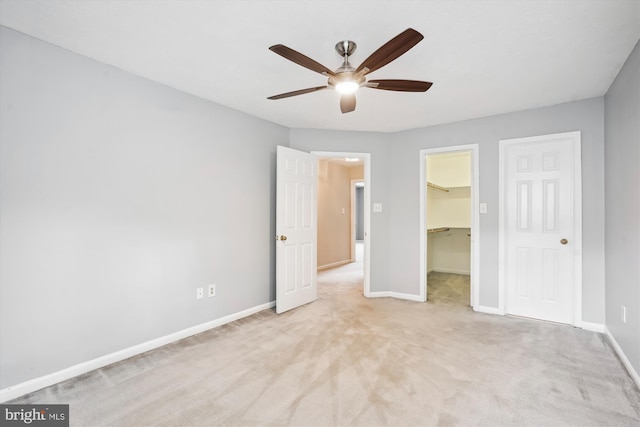 unfurnished bedroom featuring a closet, a spacious closet, ceiling fan, carpet, and baseboards