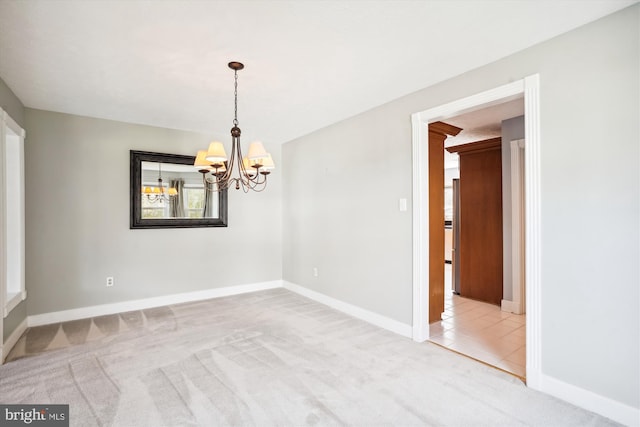 empty room with baseboards, a notable chandelier, and light colored carpet