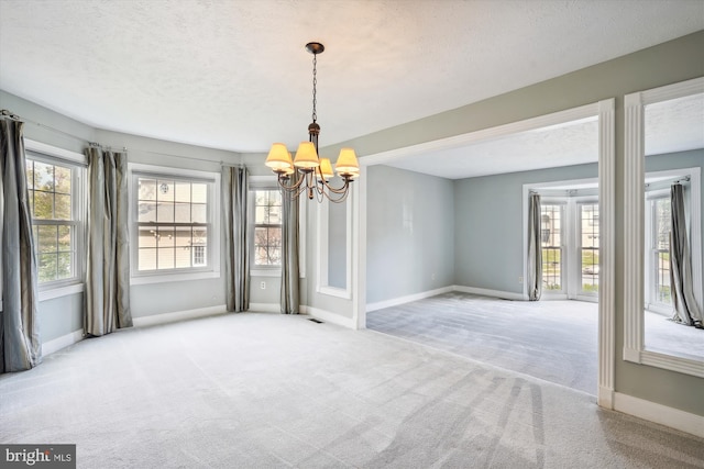 unfurnished dining area with carpet floors, a textured ceiling, baseboards, and an inviting chandelier