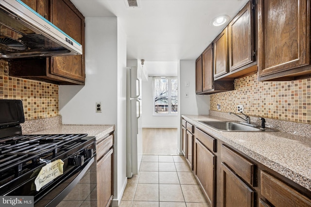 kitchen with under cabinet range hood, a sink, gas stove, light tile patterned flooring, and light countertops