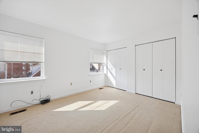 unfurnished bedroom with carpet flooring, visible vents, and multiple closets