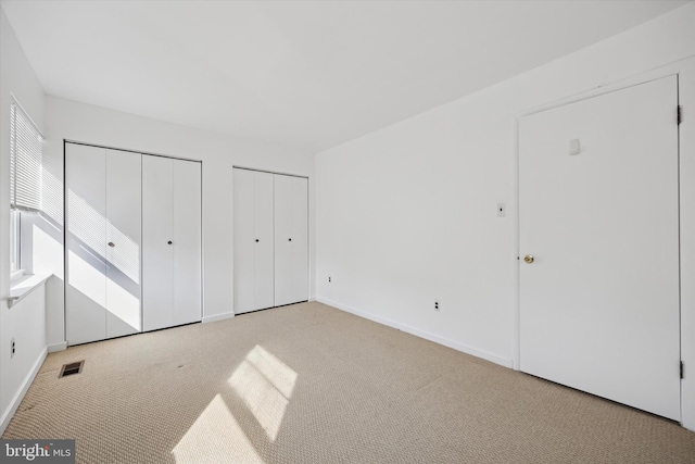 unfurnished bedroom with visible vents, multiple closets, light colored carpet, and baseboards