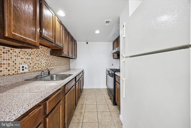 kitchen with visible vents, black gas stove, freestanding refrigerator, light tile patterned floors, and decorative backsplash