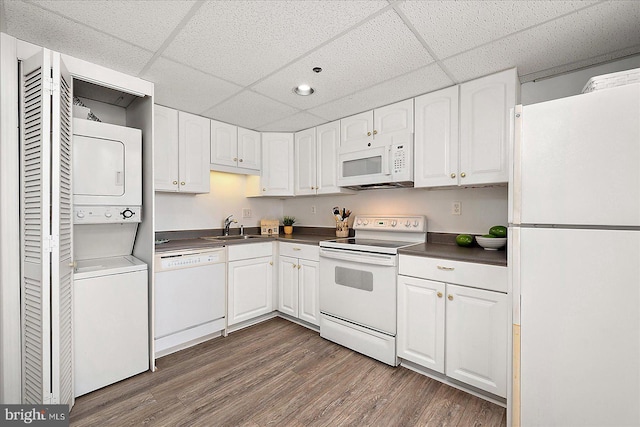 kitchen with dark countertops, white appliances, white cabinetry, stacked washer / drying machine, and dark wood-style flooring