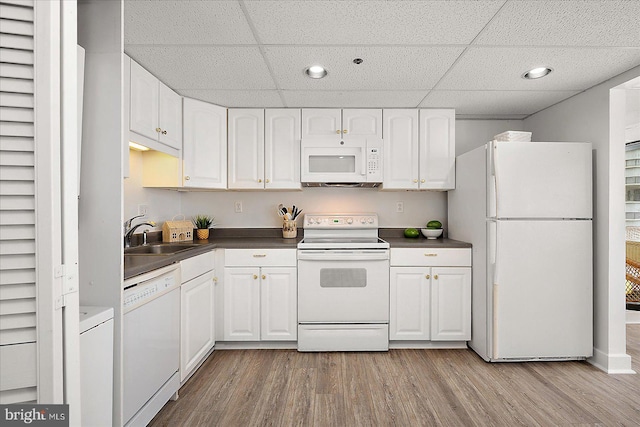 kitchen with white appliances, wood finished floors, a sink, white cabinetry, and dark countertops