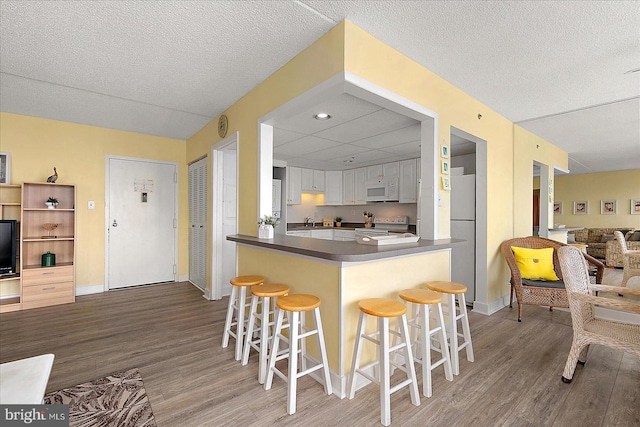 kitchen featuring a breakfast bar area, white appliances, dark countertops, and wood finished floors