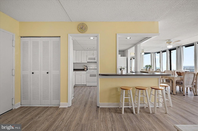 kitchen with dark countertops, a kitchen bar, wood finished floors, white cabinets, and white appliances