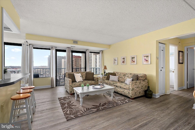 living room featuring visible vents, baseboards, a textured ceiling, and wood finished floors