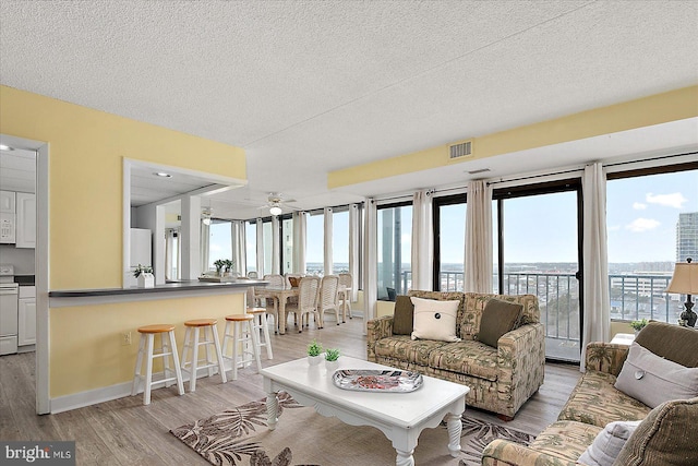 living area featuring light wood finished floors, visible vents, baseboards, ceiling fan, and a textured ceiling