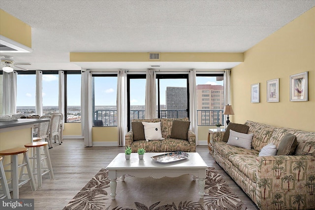 living room featuring visible vents, baseboards, light wood-style floors, a textured ceiling, and a ceiling fan