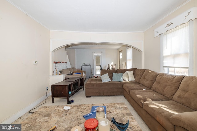 carpeted living area with arched walkways, baseboards, and ornamental molding