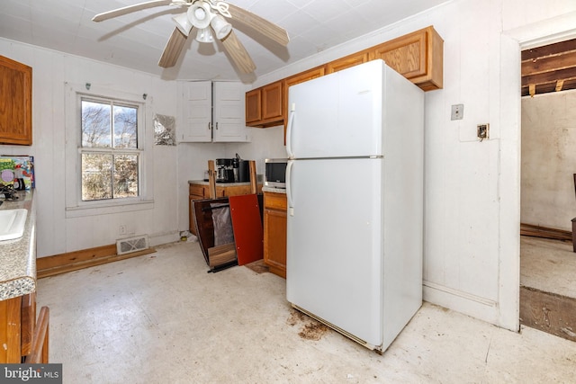 kitchen with visible vents, stainless steel microwave, freestanding refrigerator, brown cabinetry, and light countertops