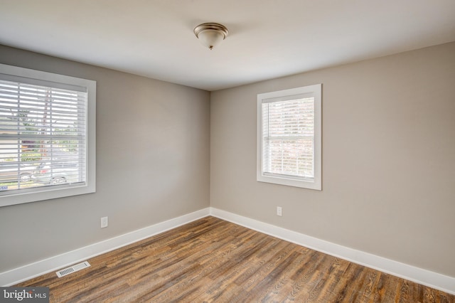 spare room with visible vents, plenty of natural light, baseboards, and wood finished floors